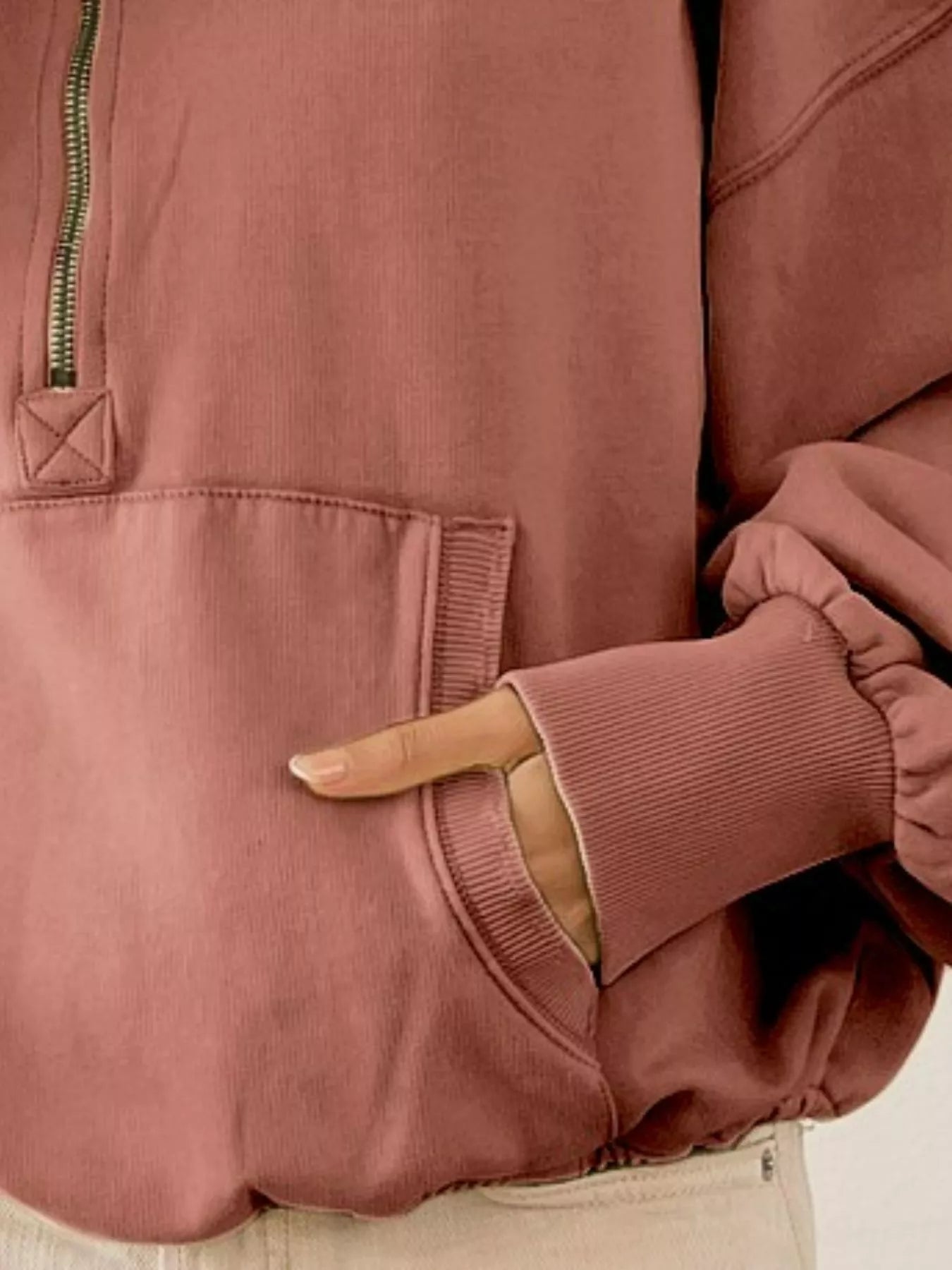 Detail shot of the BiBi terracotta color half zip fleece hoodie showing the pocket, zipper and sleeve cuff.